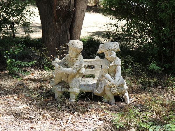 Garden statue of two children reading on a bench under a tree